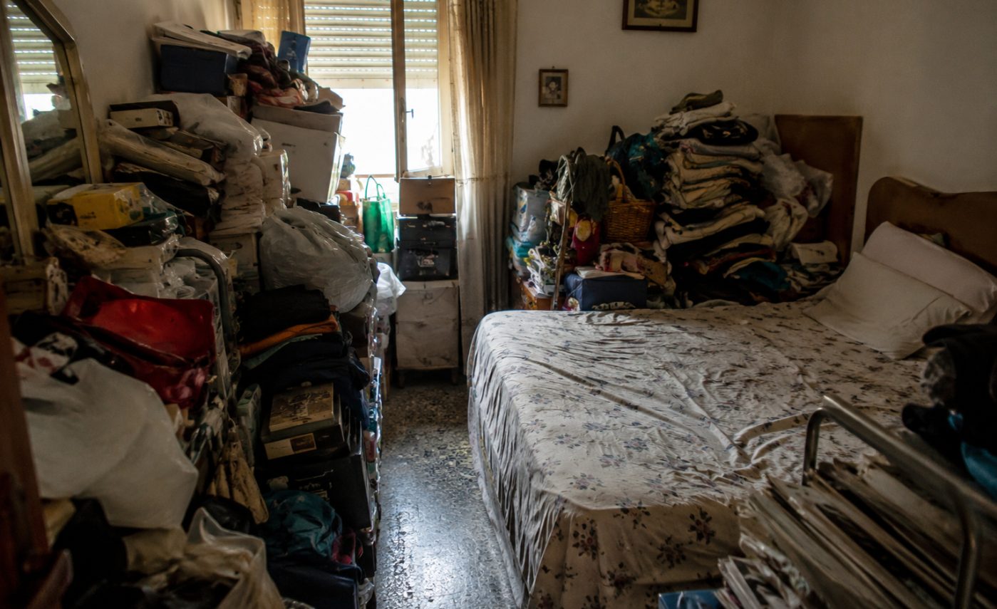 Camera da letto invasa da pile di scatole e vestiti in una situazione di disturbo da accumulo